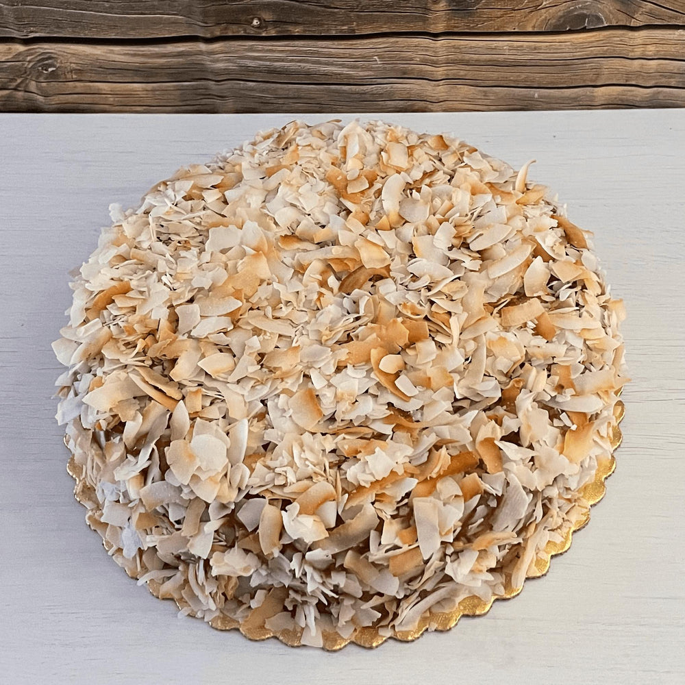 Gluten-free, sugar-free, dairy-free Coconut Full Life Cake topped with sugar-free caramel syrup and golden brown toasted coconut flakes, offering a taste of tropical indulgence.Full Life Gourmet Bakery